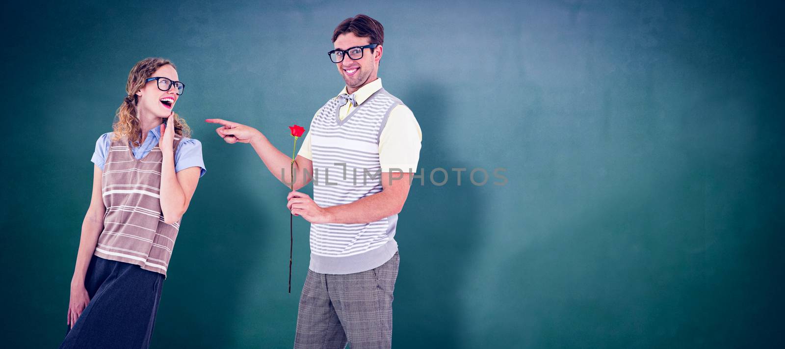 Geeky hipster holding rose and pointing his girlfriend  against green chalkboard