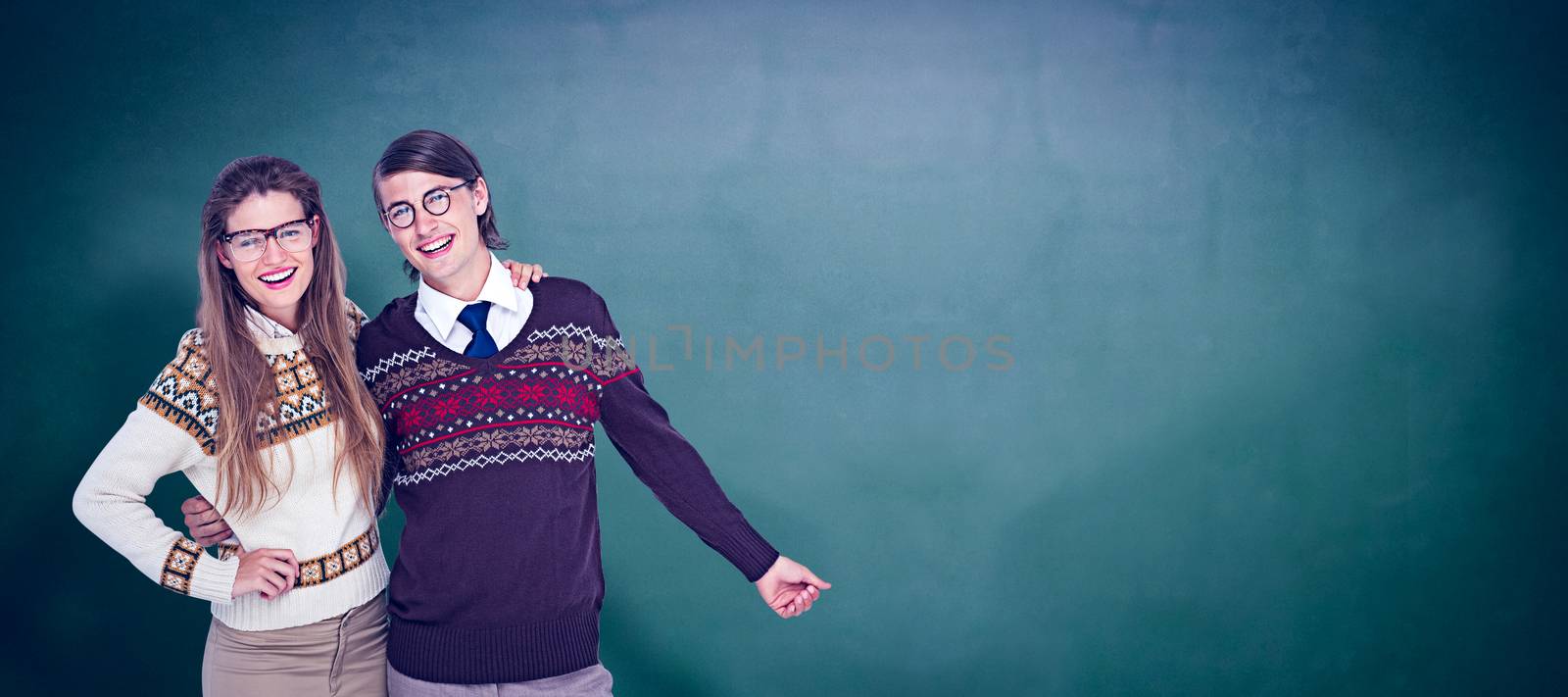 Happy geeky hipster couple embracing against green chalkboard