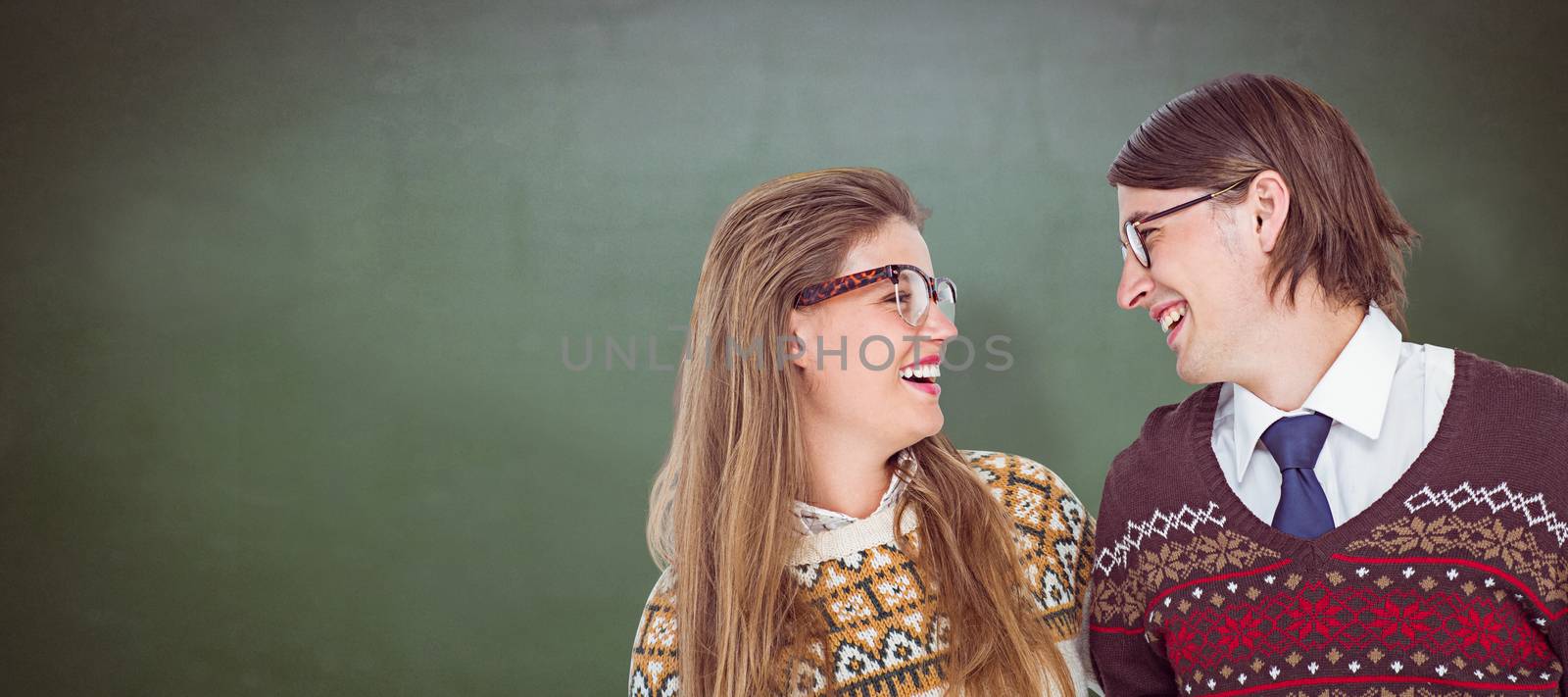 Happy geeky hipster couple looking at each other against green chalkboard