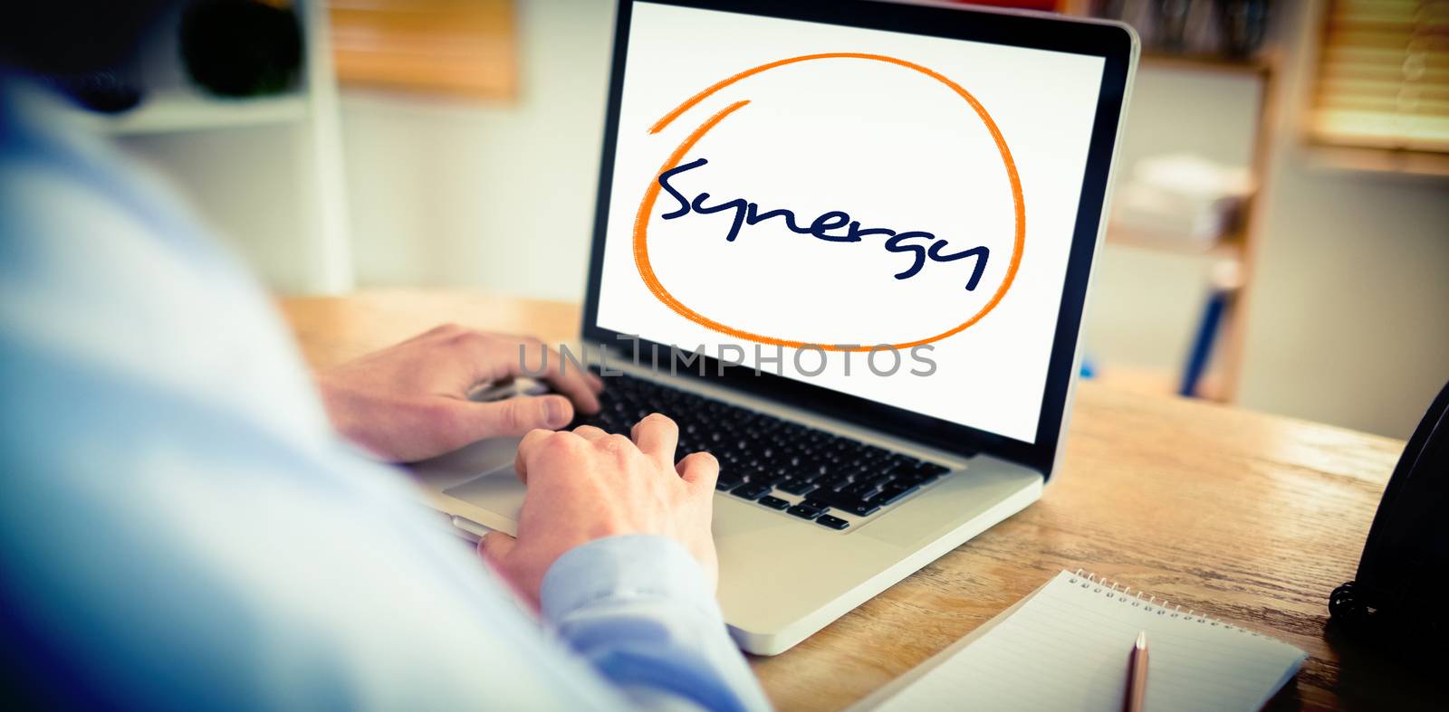 The word synergy against businessman working on his laptop
