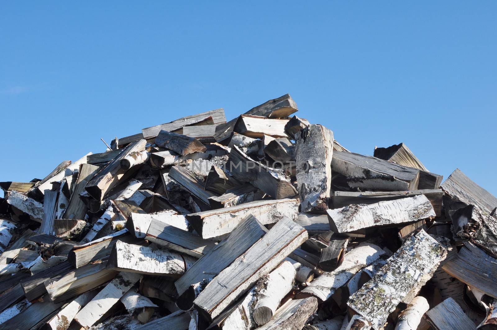 A Pile of Dry Chopped Cleaving Birch Firewood Against the Blue Sky