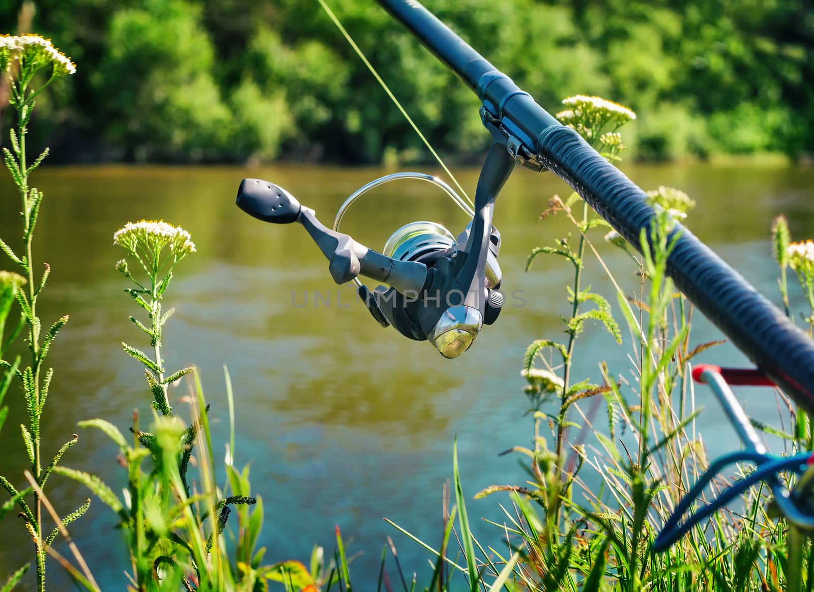 On the banks of the beautiful river above the water feeder installed - English fishing tackle for catching fish comfortable with the rod and the reel.