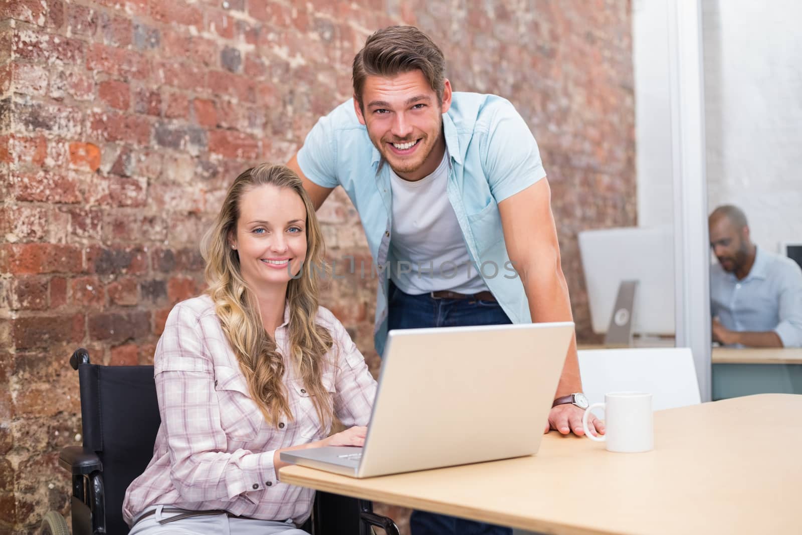 Smiling businesswoman in wheelchair working with colleague in the office