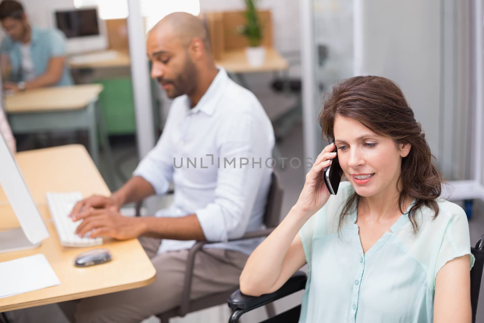 Smiling businesswoman in wheelchair on the phone in front of his colleague in the office