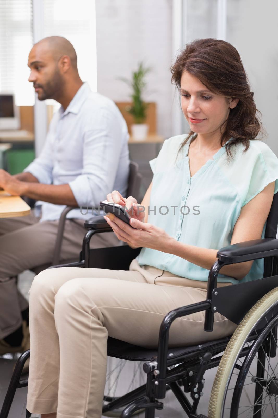 Businesswoman in wheelchair texting on phone in the office