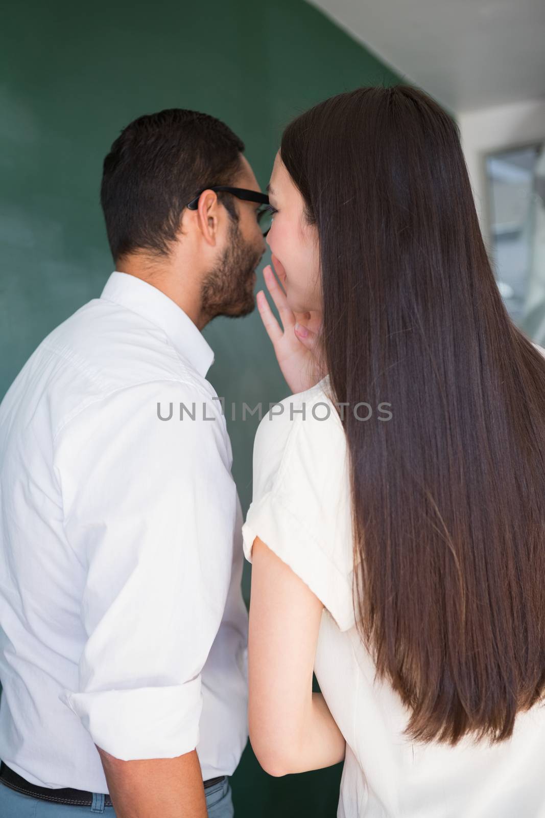 Young businesswoman whispering into male colleagues ear at office