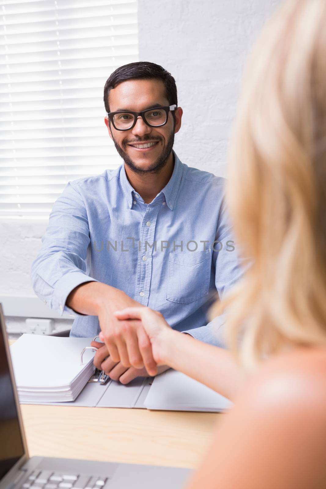 Young businessman shaking hands with woman during interview in office