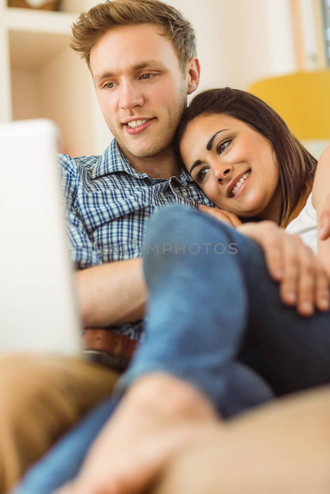 Happy young couple relaxing on the couch with laptop by Wavebreakmedia