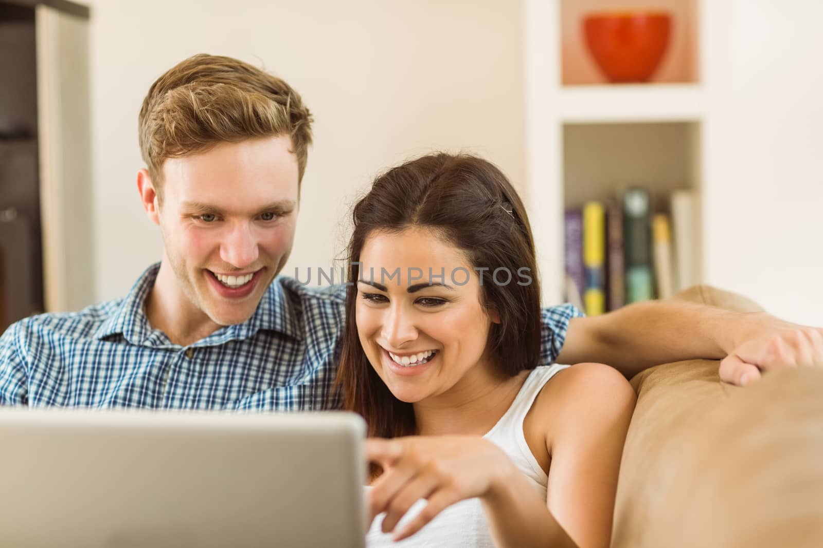 Happy young couple relaxing on the couch with laptop by Wavebreakmedia