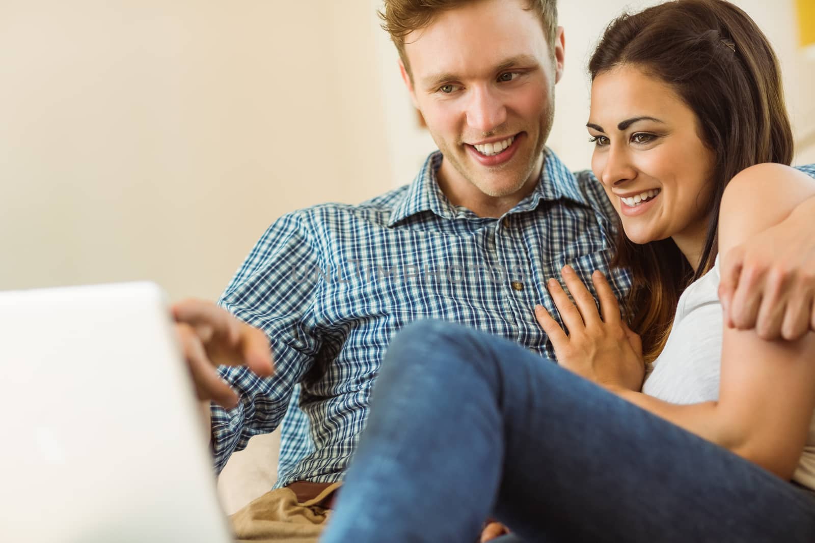 Happy young couple relaxing on the couch with laptop at home in the living room