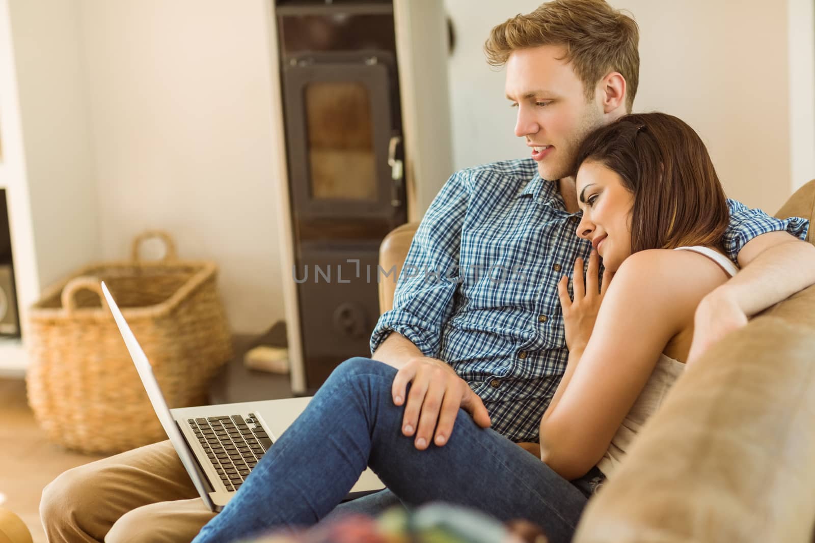 Happy young couple relaxing on the couch with laptop at home in the living room