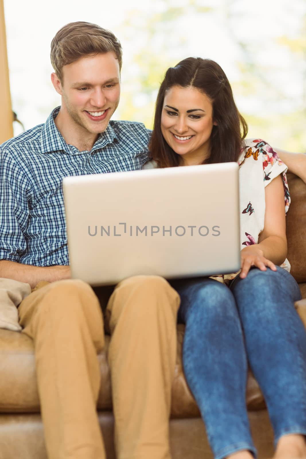 Young cute couple relaxing on couch with laptop by Wavebreakmedia