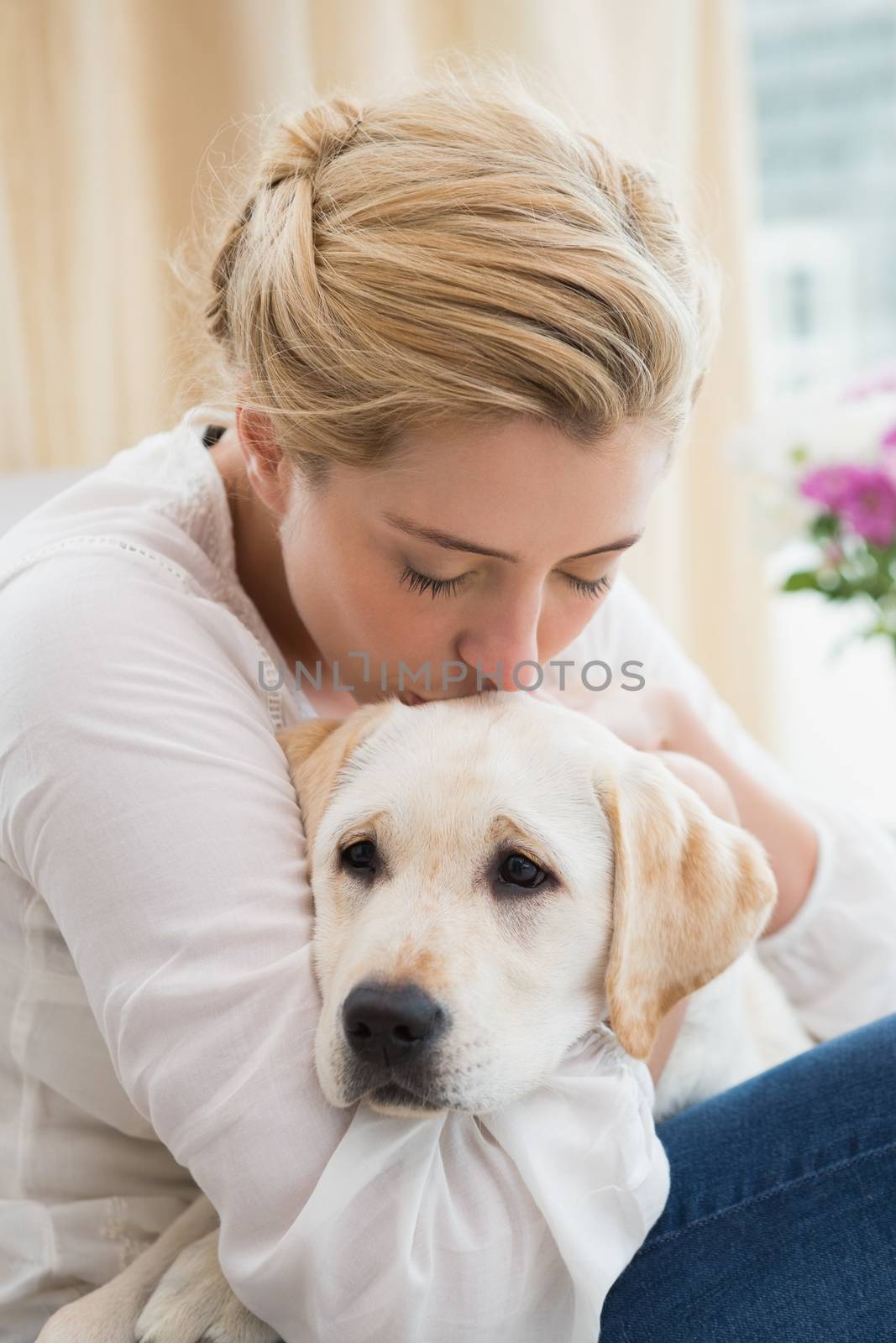 Happy blonde cuddling with puppy on sofa by Wavebreakmedia