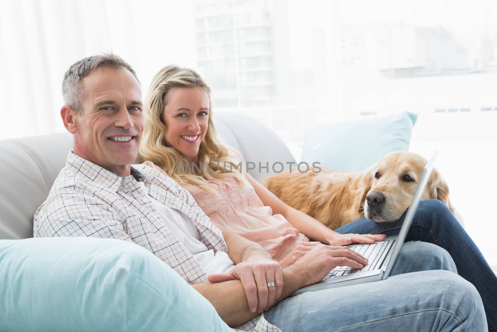 Couple using laptop and spending time with their dog at home in the living room