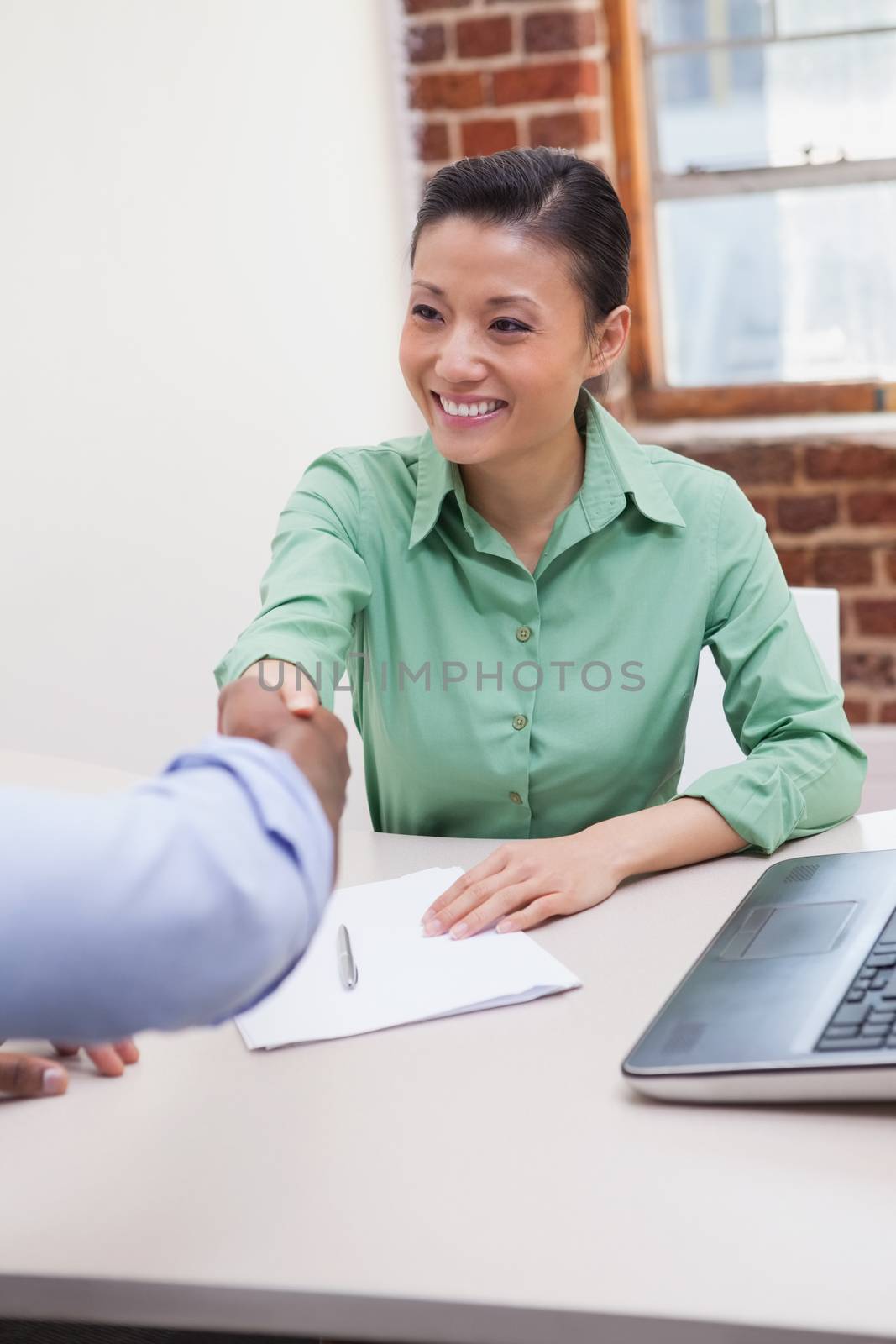 Casual business people shaking hands at desk by Wavebreakmedia