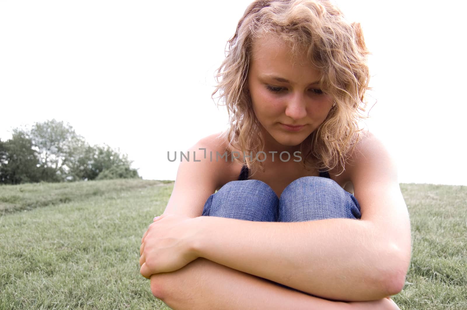 Young depressed girl sitting on a grass in park.