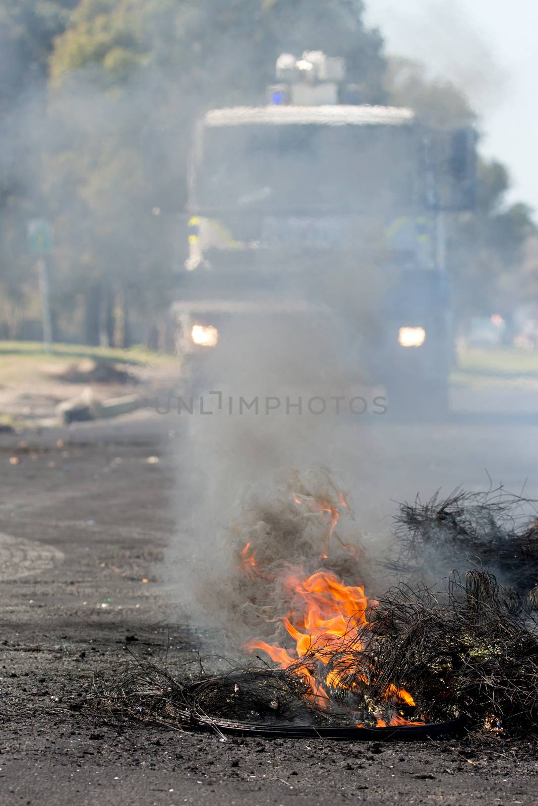 Burning rubber tyres in the streets in South Africa with police riot vehicle in the backround
