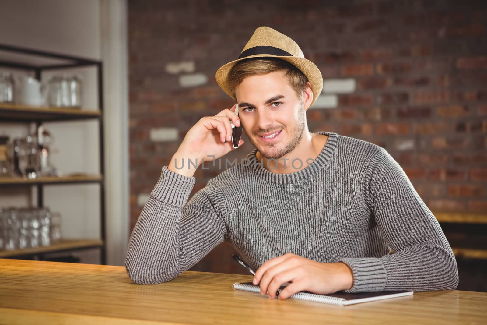 Portrait of handsome hipster phoning and holding pen at coffee shop