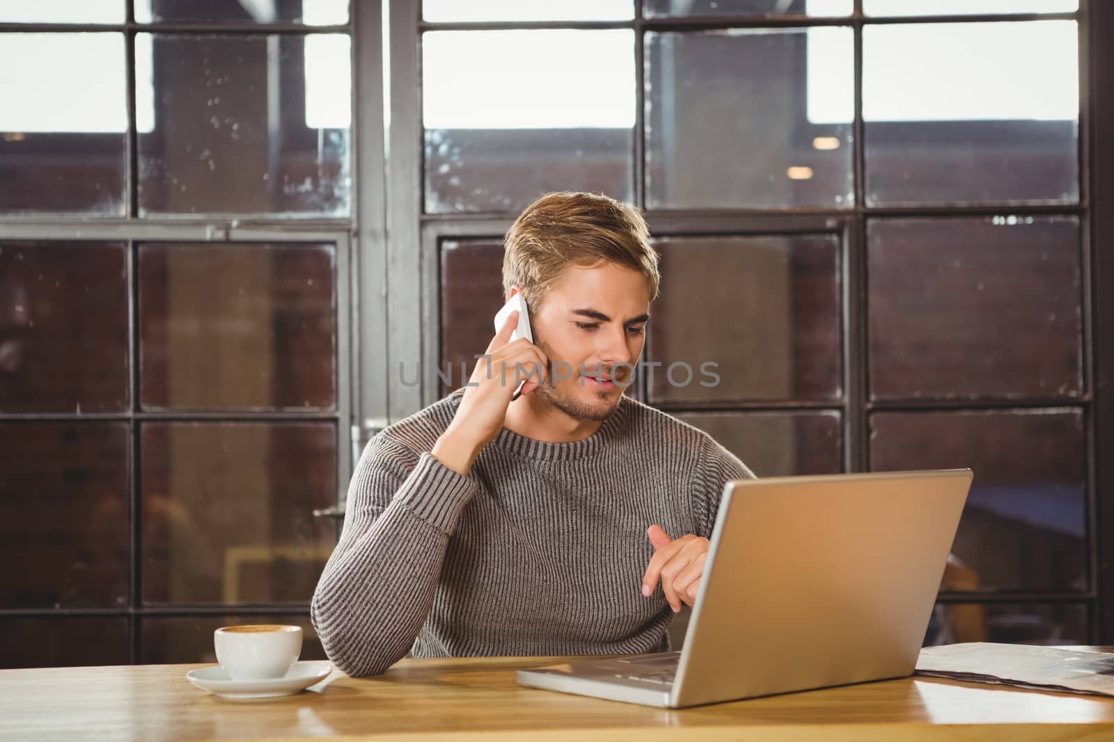 Handsome man phoning and looking at laptop by Wavebreakmedia