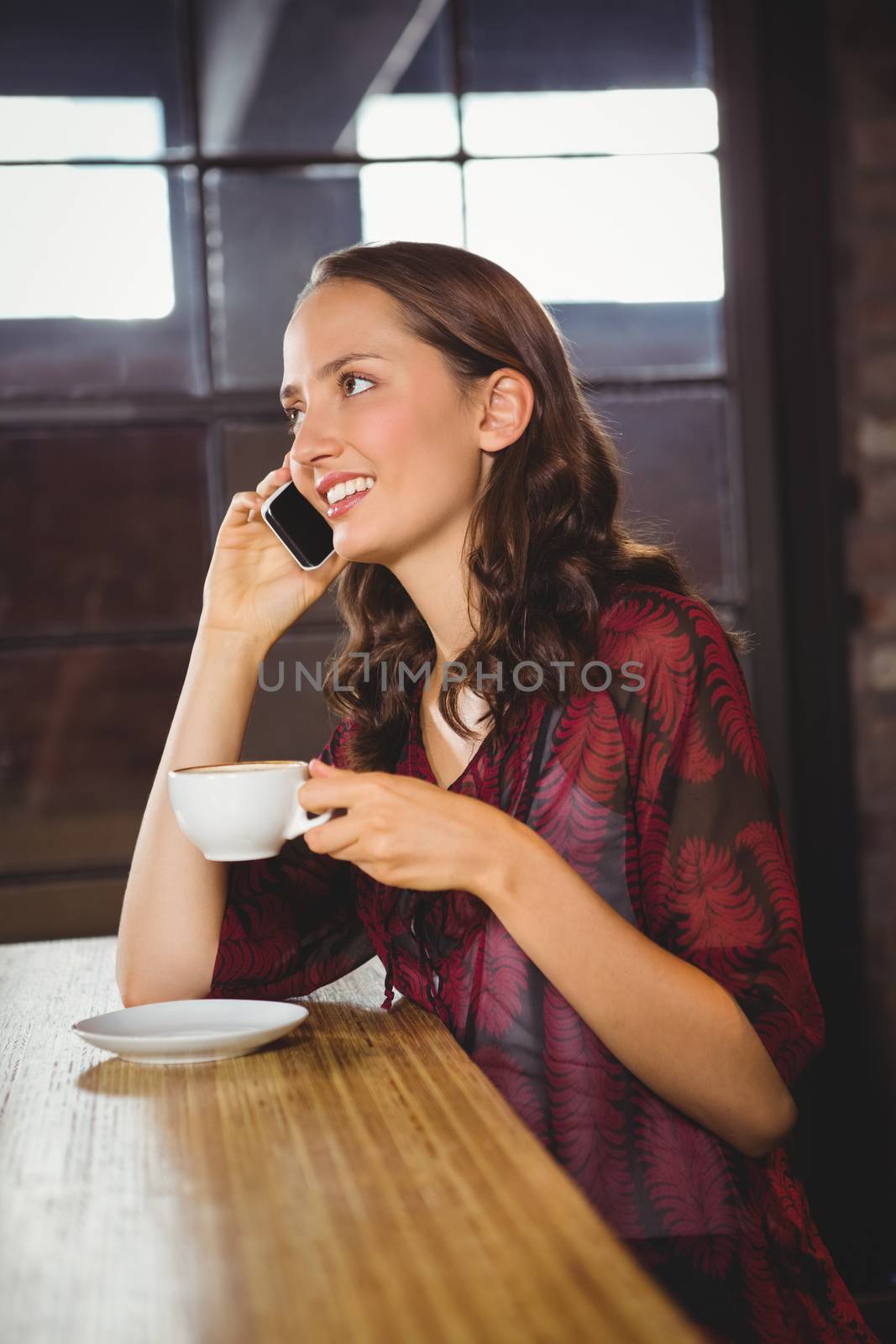 Smiling brunette drinking coffee and phoning at coffee shop