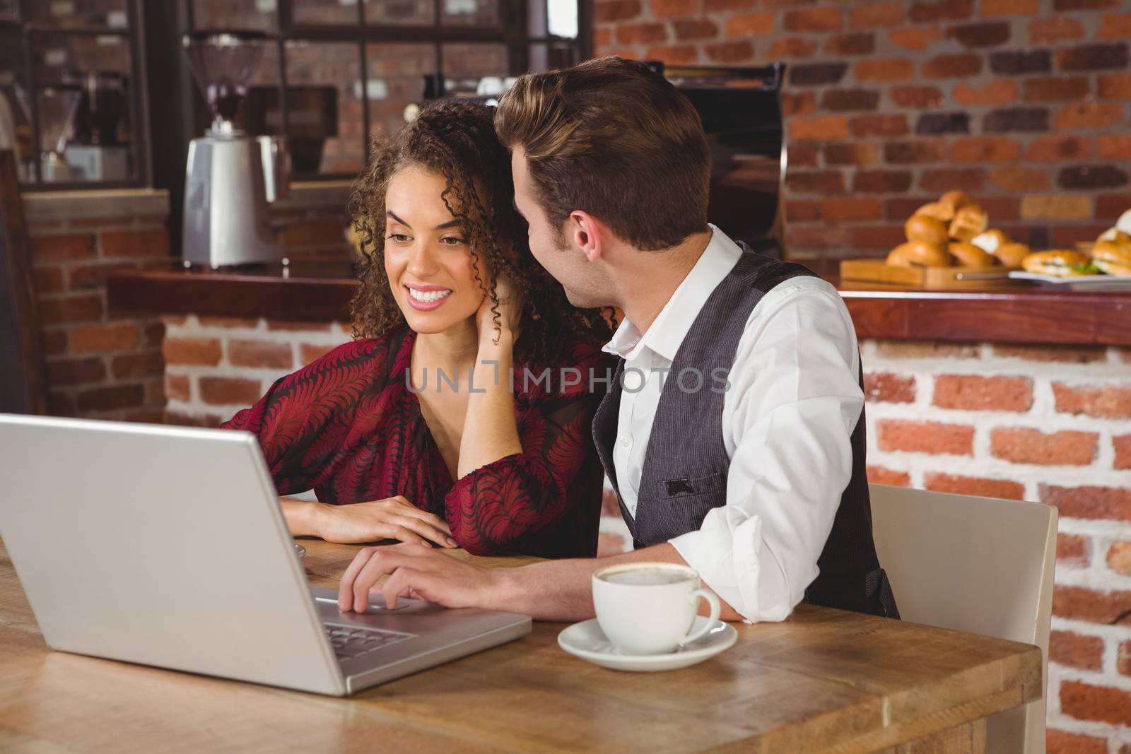 Cute couple on a date watching photos on a laptop at the cafe