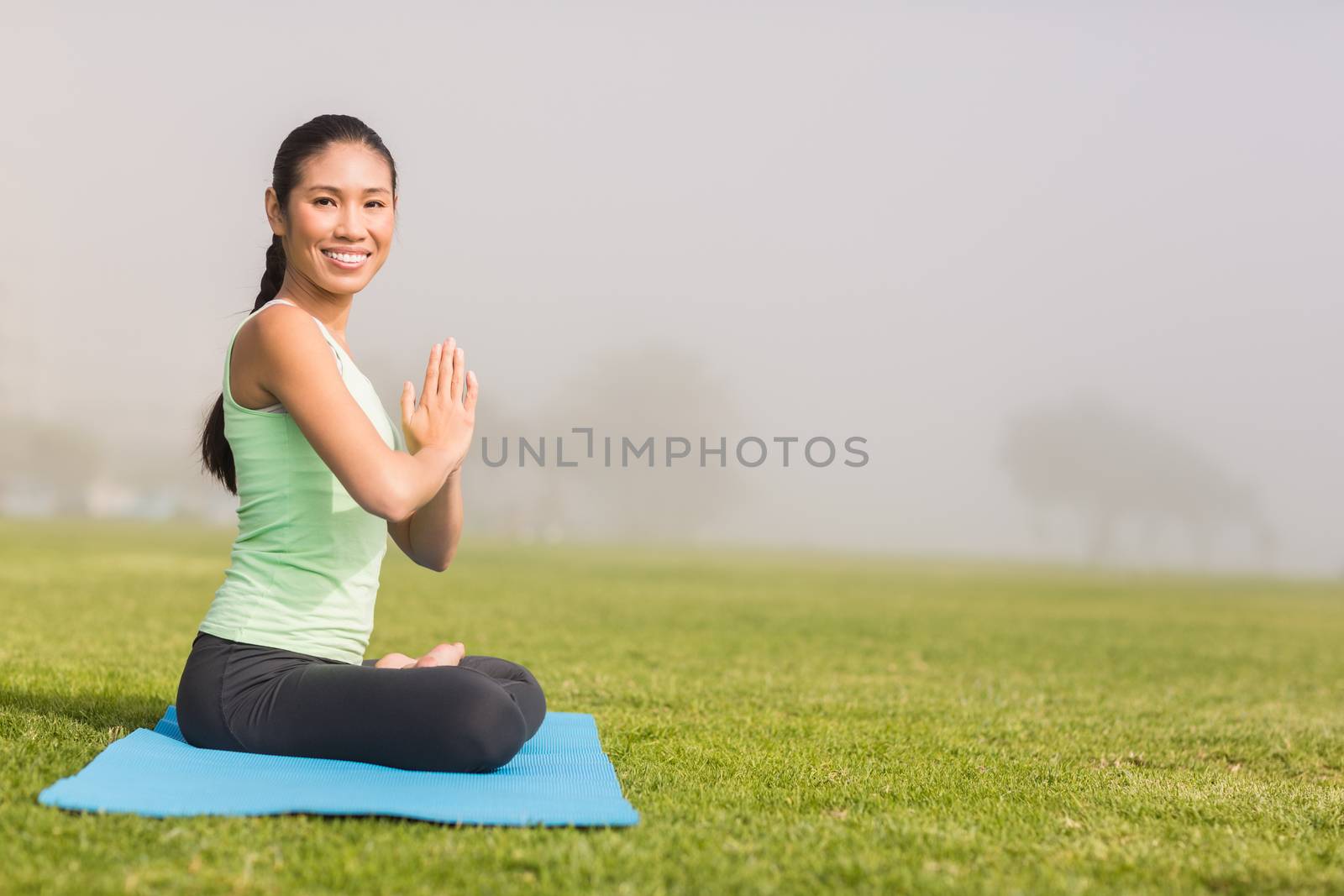 Portrait of smiling sporty woman doing the lotus pose in parkland