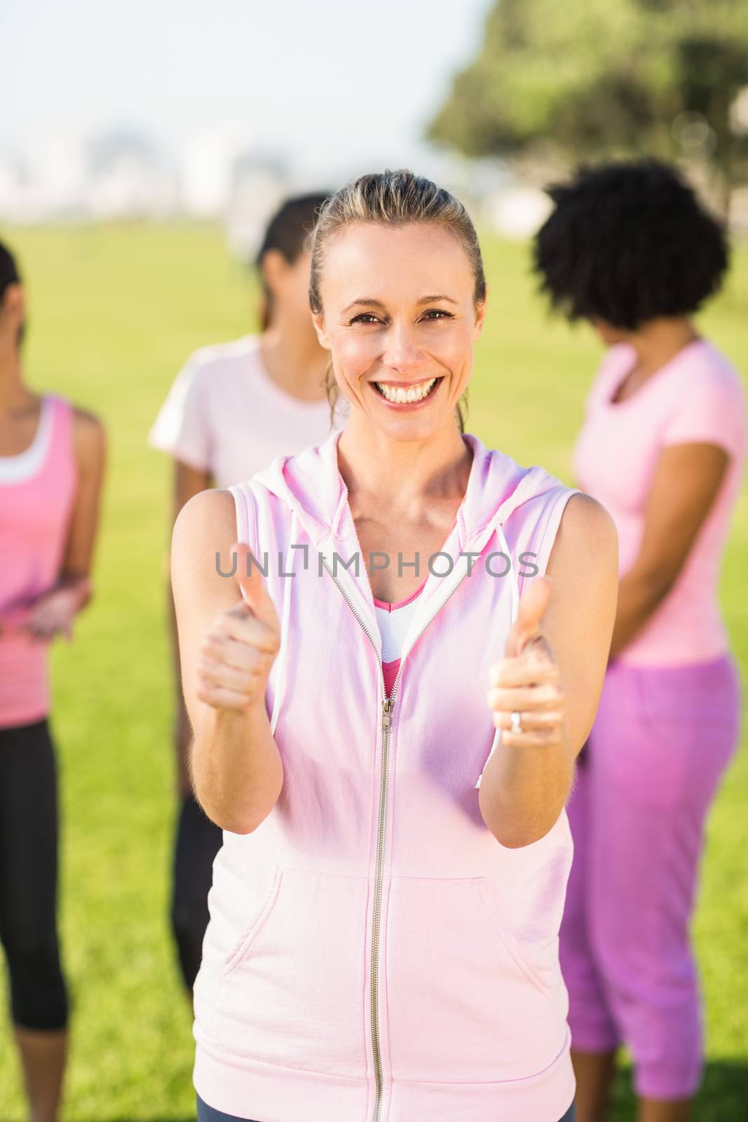 Portrait of smiling blonde wearing pink for breast cancer in front of friends in parkland