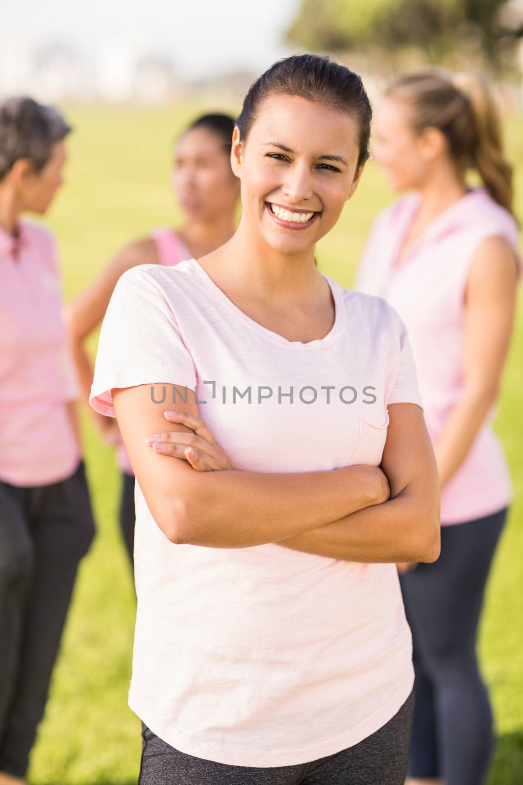 Portrait of smiling brunette wearing pink for breast cancer in front of friends in parkland