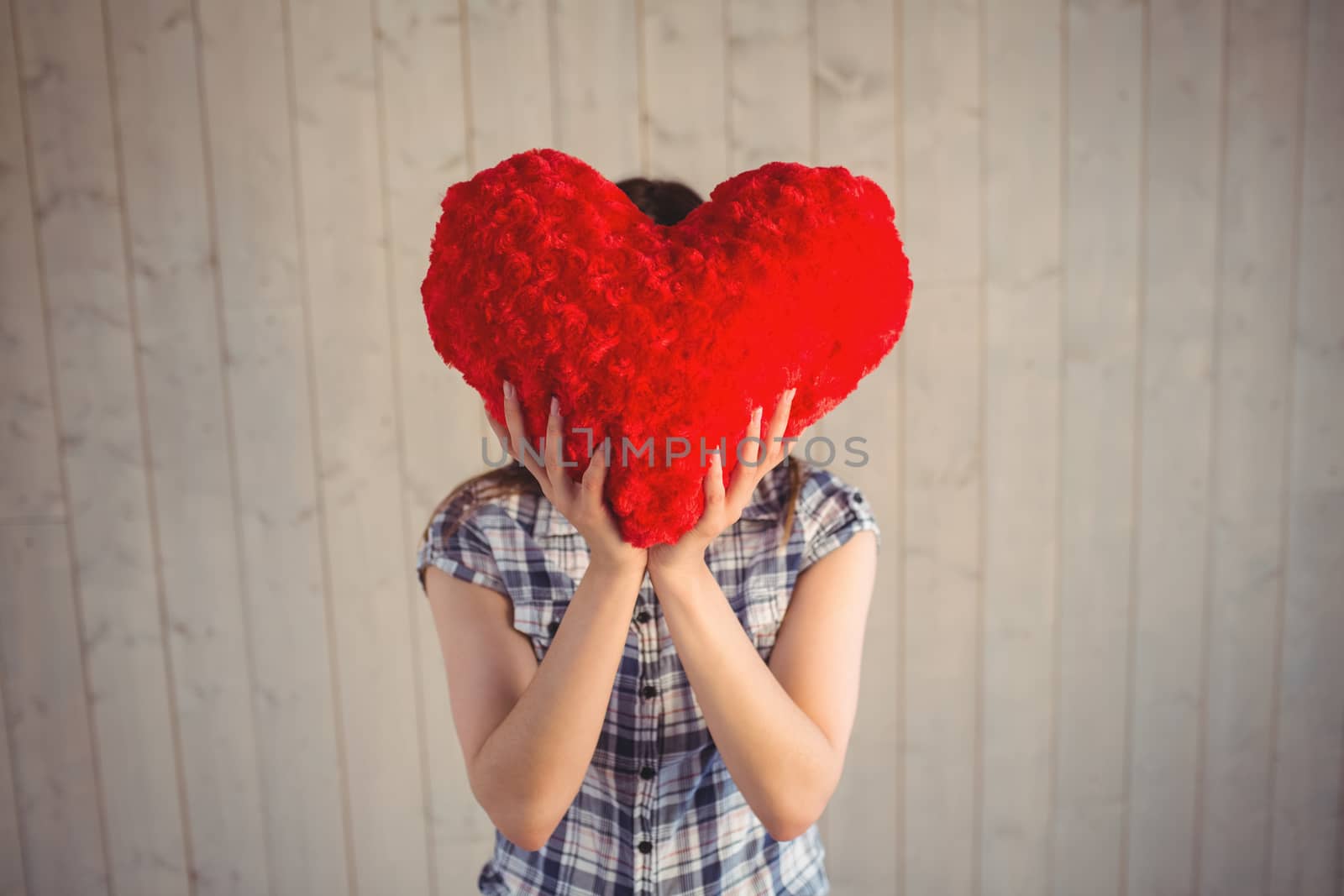 Pretty hipster holding heart pillow on wooden planks background