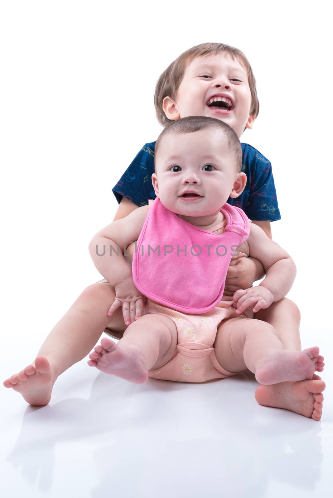 A happy young boy and his baby sister smiling and hugging on a white background.