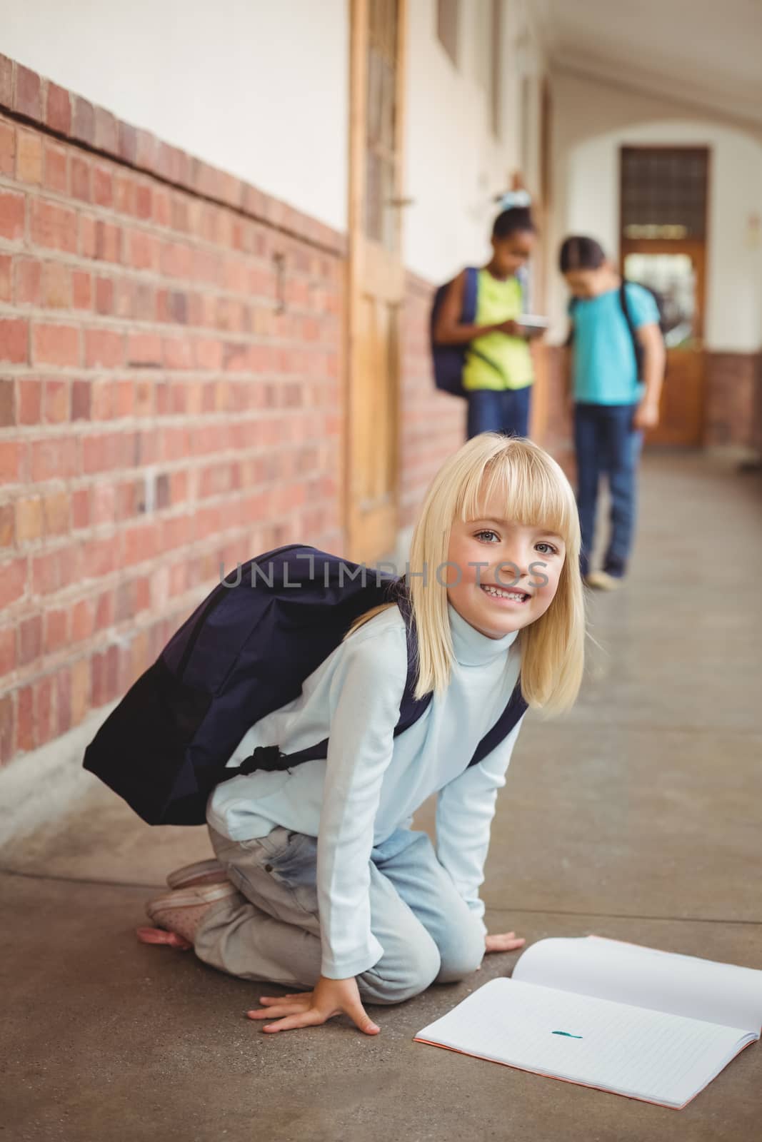 Cute pupil kneeling over notepad at corridor by Wavebreakmedia