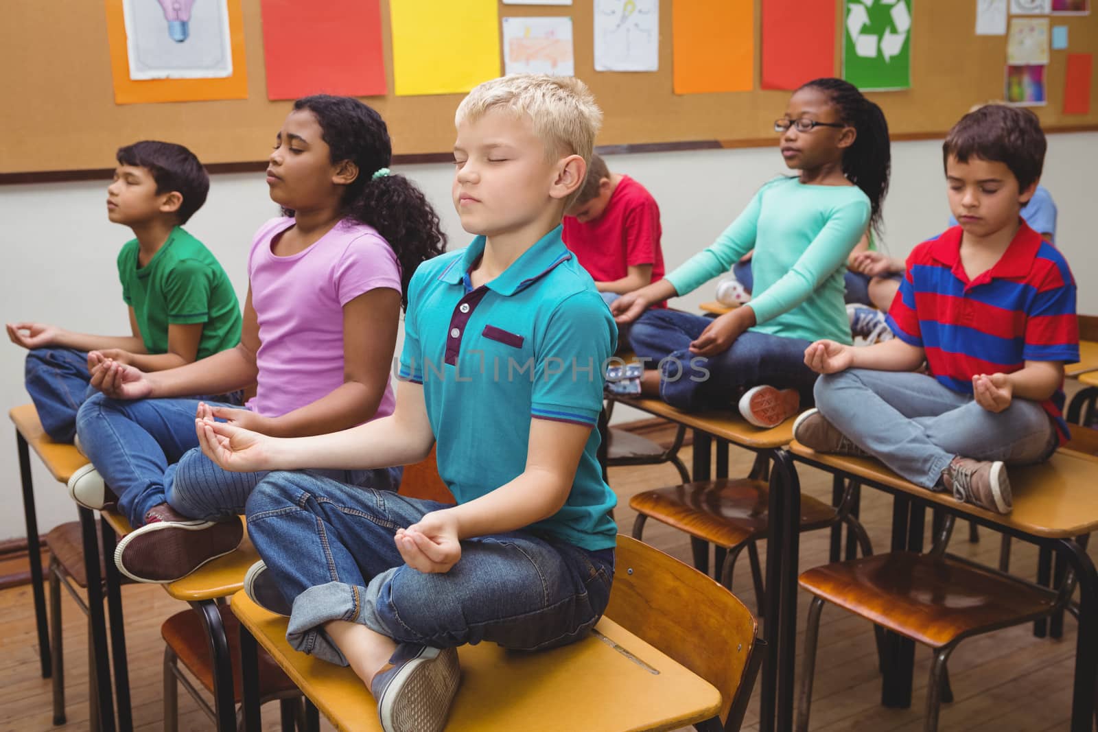 Pupils meditating on classroom desks by Wavebreakmedia