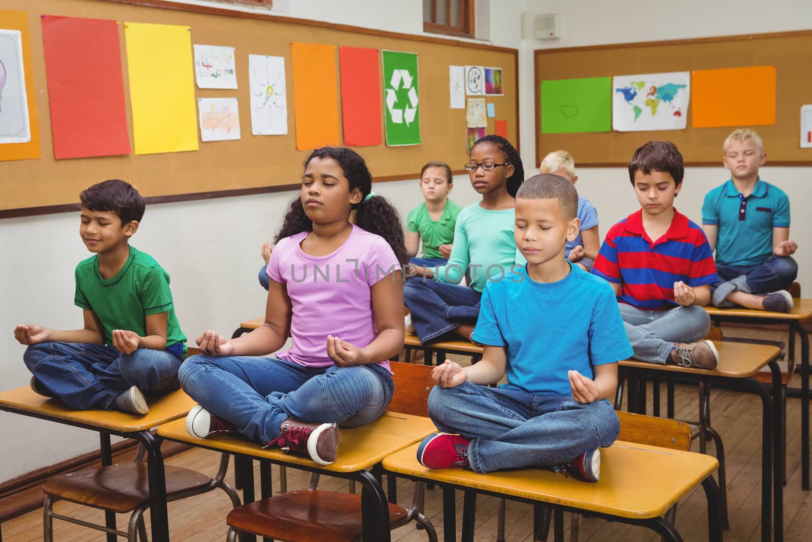 Pupils meditating on classroom desks by Wavebreakmedia