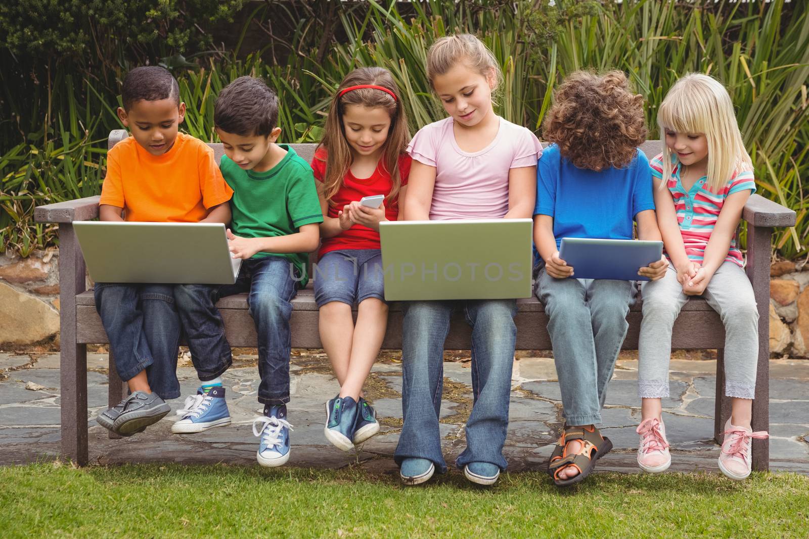 Kids sitting on a park bench with laptops