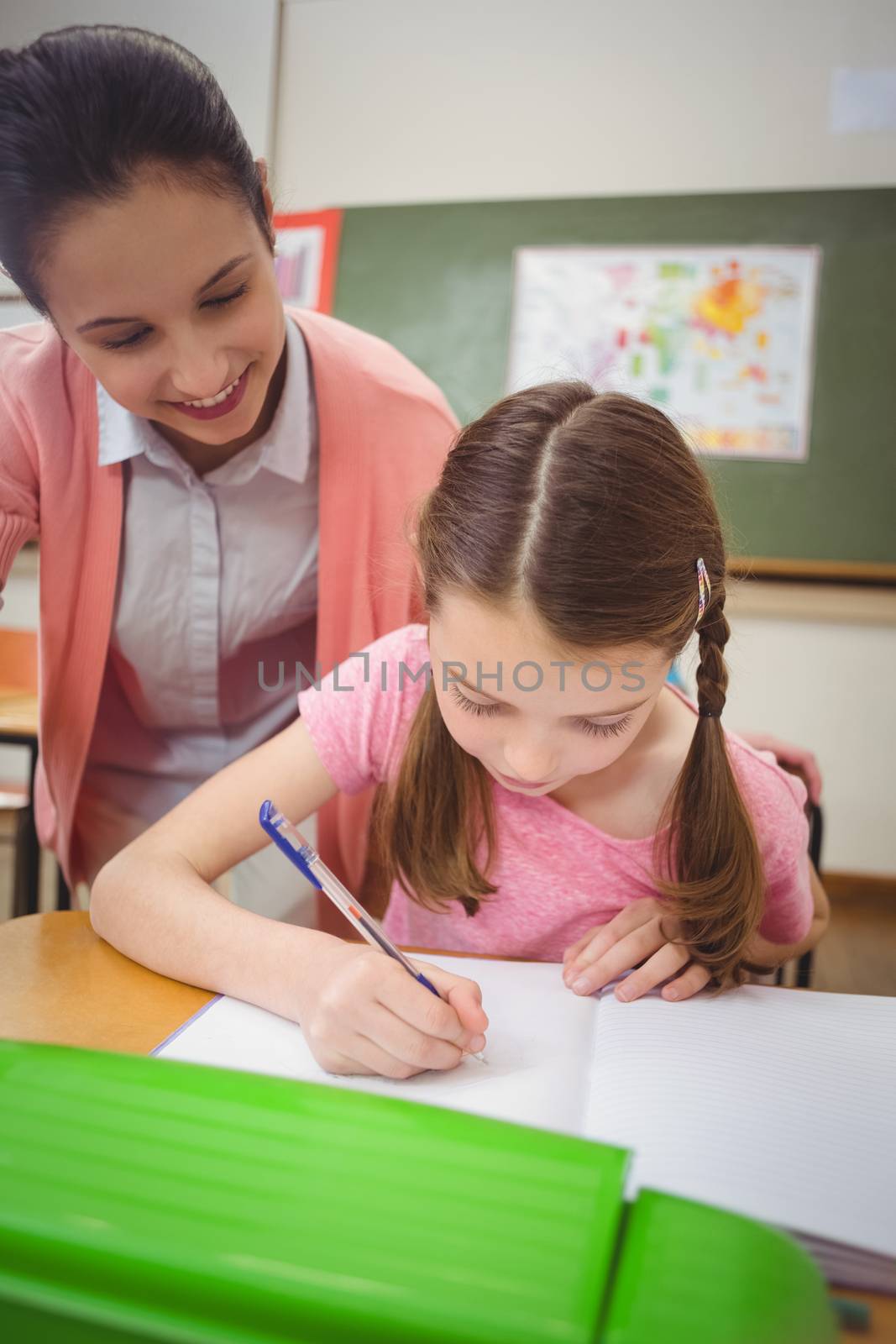 Pupil and teacher at desk in classroom at the elementary school