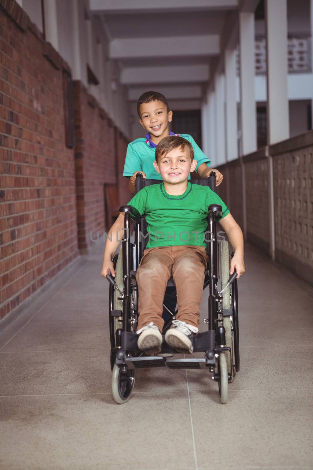 Smiling student in a wheelchair and friend pushing on the elementary school grounds