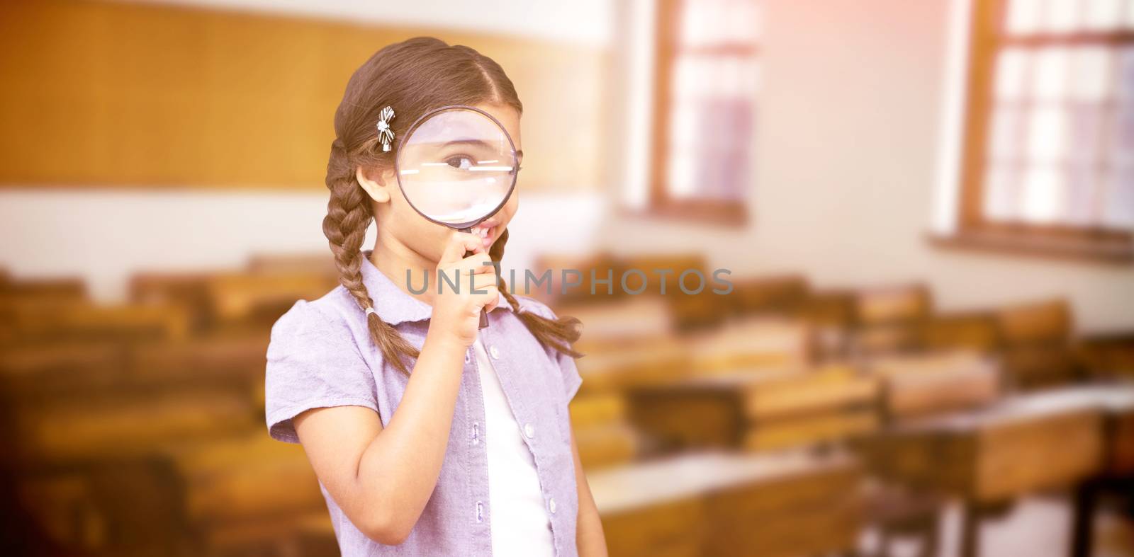 Pupil looking through magnifying glass against empty classroom