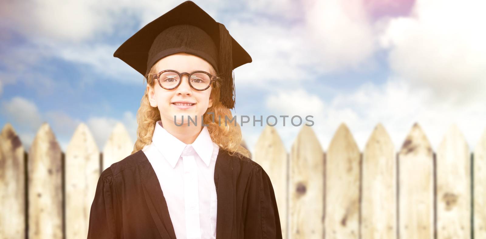 Cute pupil in graduation robe   against fence under blue sky