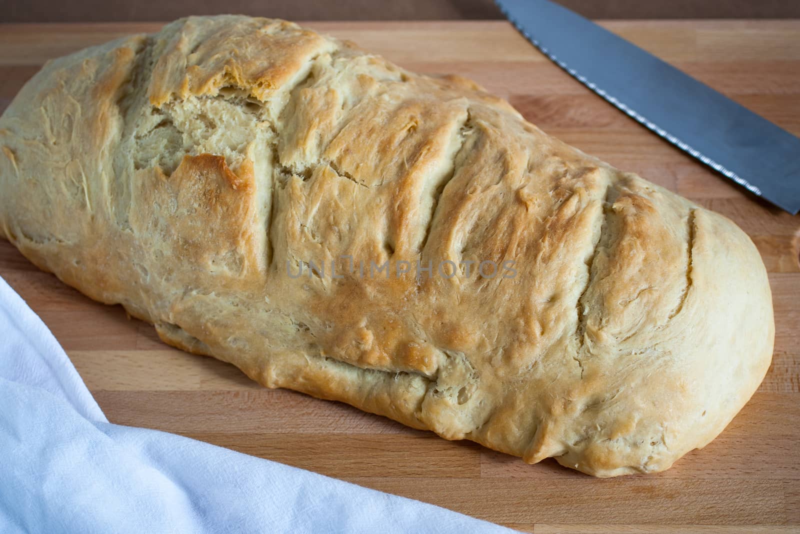 Homemade bread cooling on a cutting board with a knife and white kitchen towel nearby.
