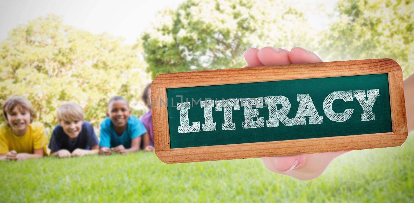 The word literacy and hand showing chalkboard against happy friends in the park 