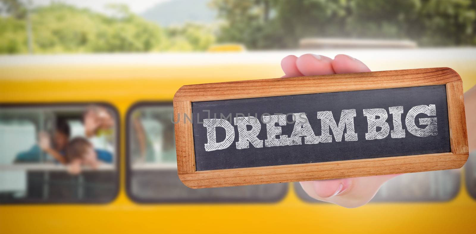 The word dream big and hand showing chalkboard against cute pupils smiling at camera in the school bus