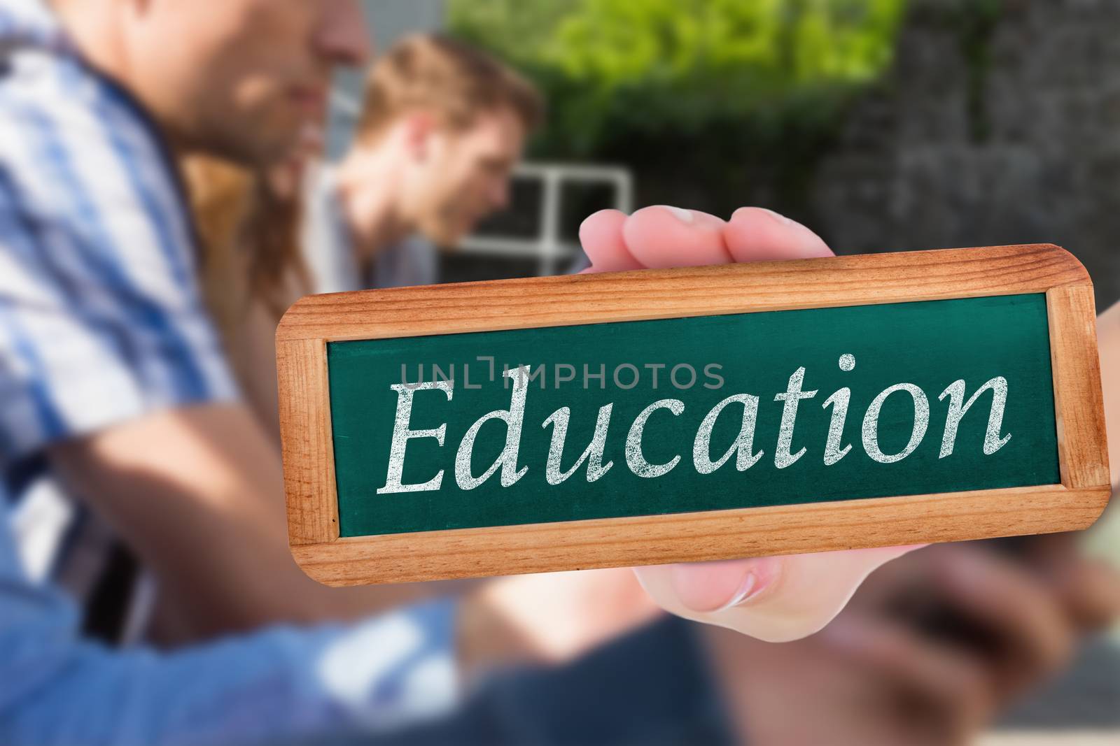 The word education and hand showing chalkboard against happy students sitting in a row texting