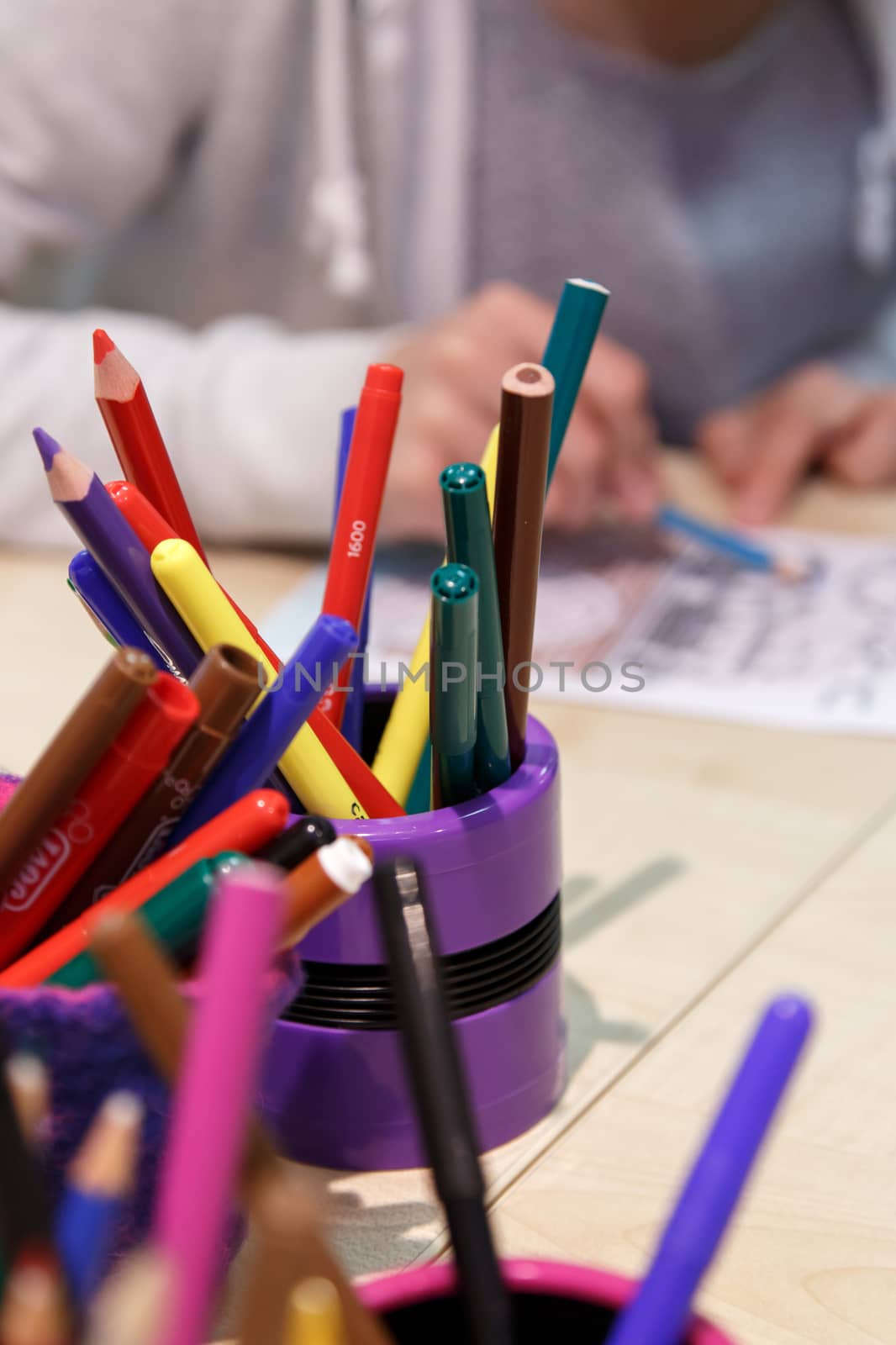 Close up detailed view of heap of multicolored dry paint pencils in pencilcases, with a painting child background.