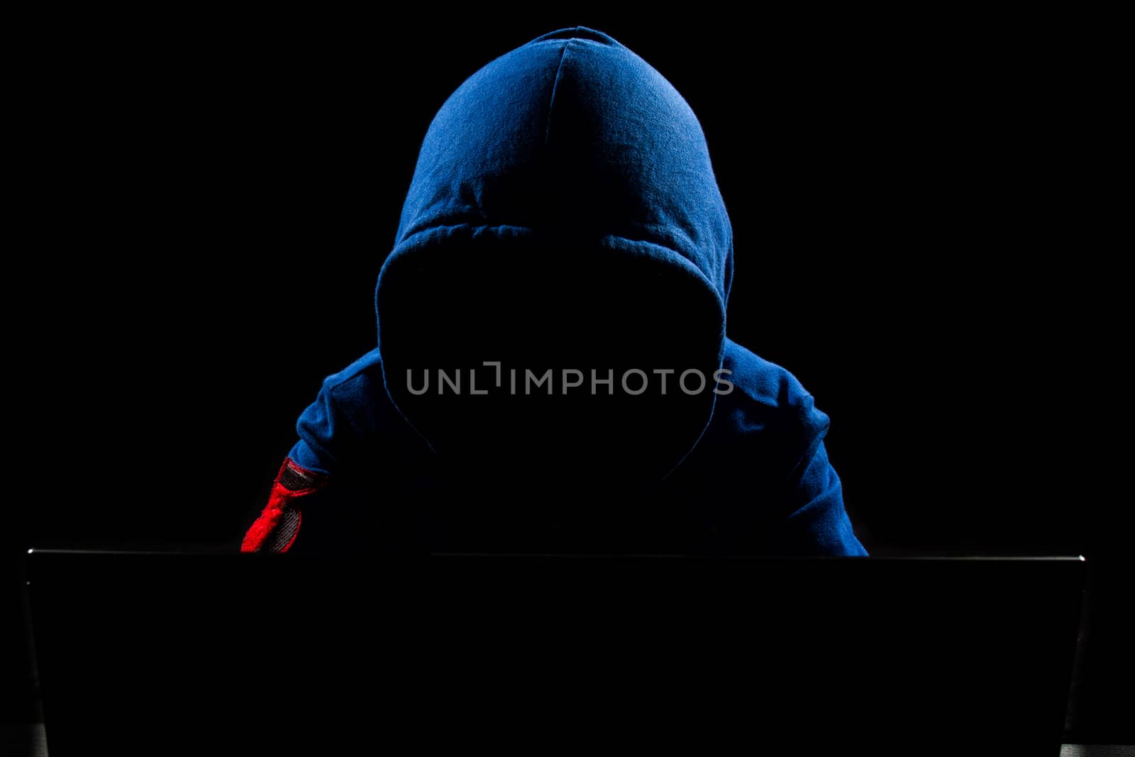 Faceless hacker with laptop in black isolated background.