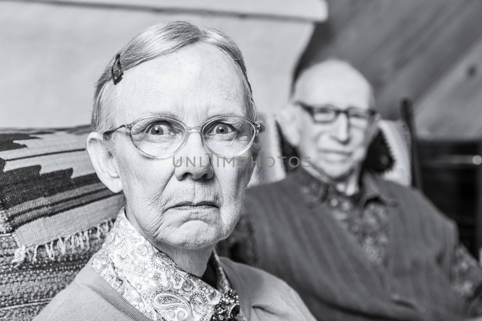 Elderly scowling couple seated in indoors woman