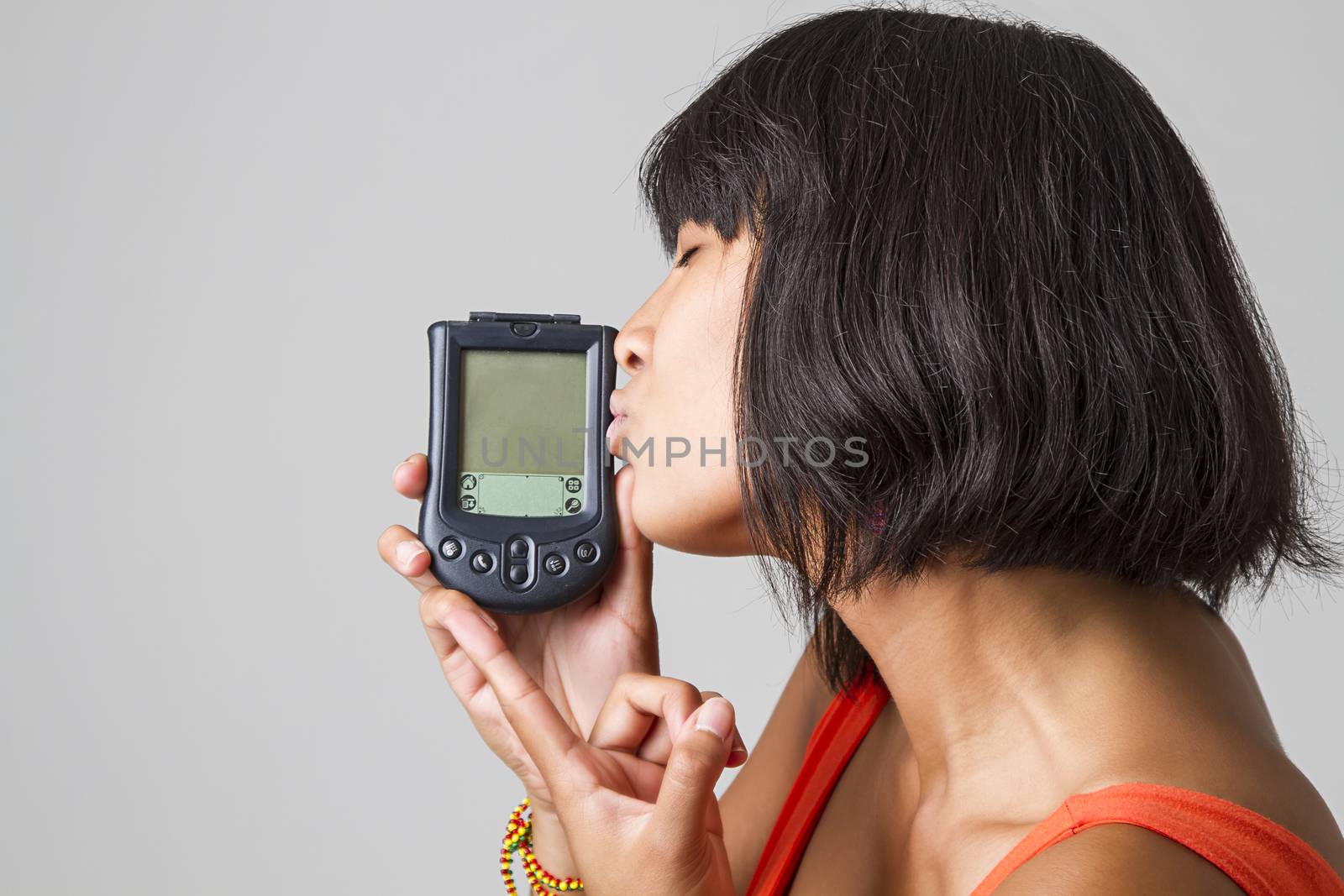 Philipino woman wearing a low cut orange dress kissing an old digital personnal assistant