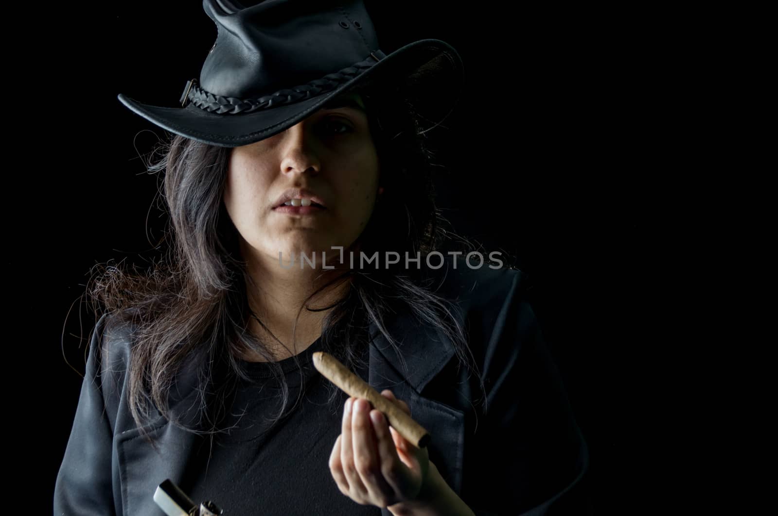 Young girl with a cigar in her mouth wearing black leather jacket and hat and looking at the camera