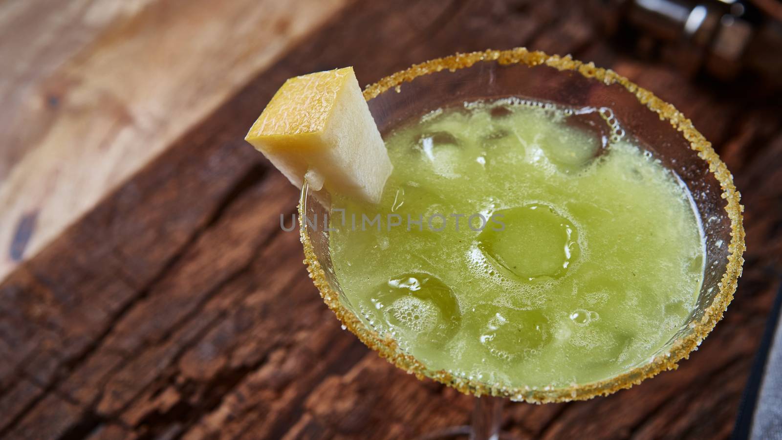 Green margarita melon cocktail with copy space on wooden background.
