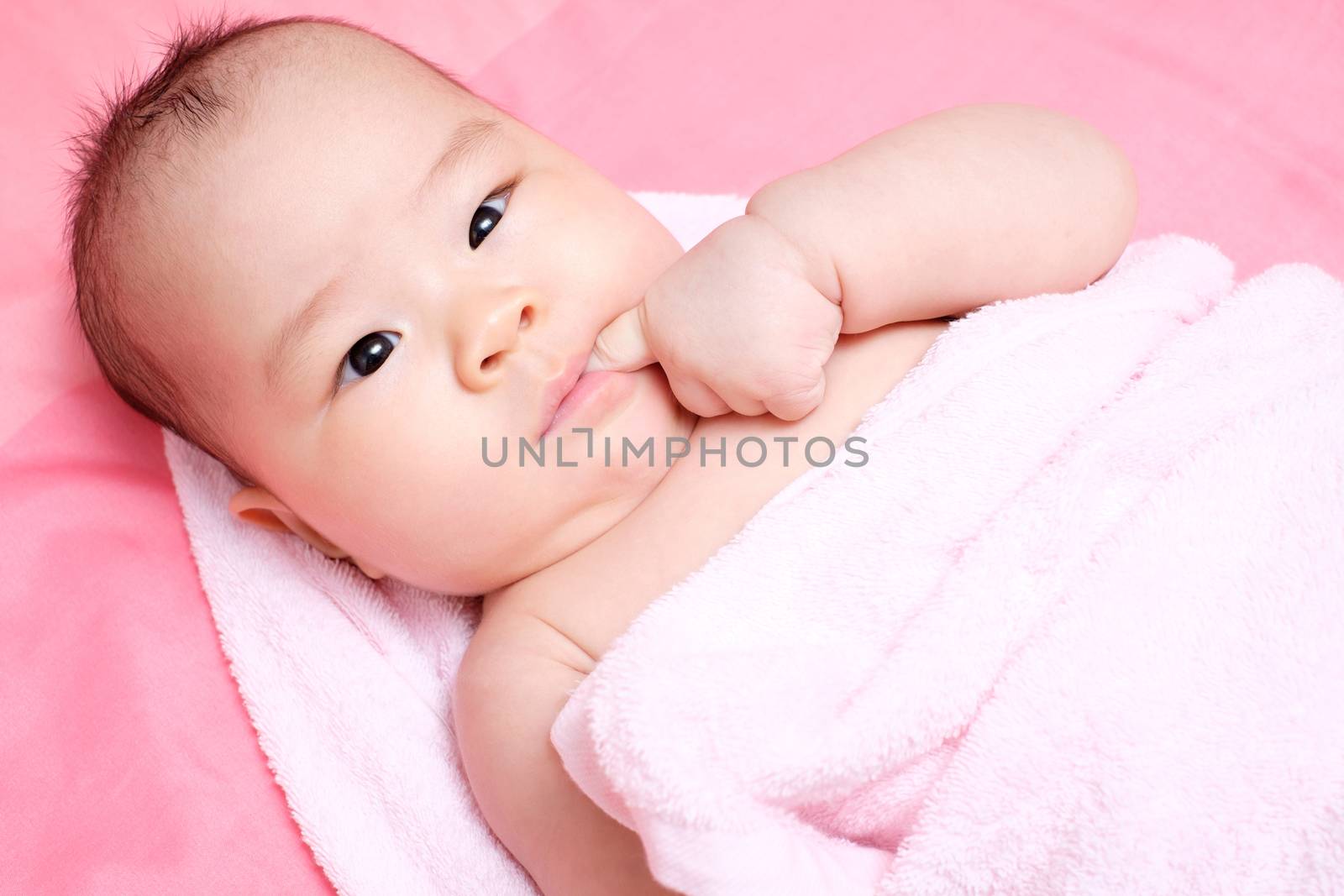 Asian baby girl whit pink towel, put her finger in her mouth