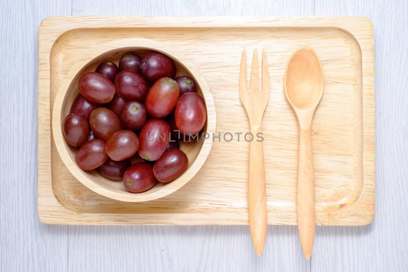 Red grapes in wooden bowl and spoon. they on white wooden table. Clear light